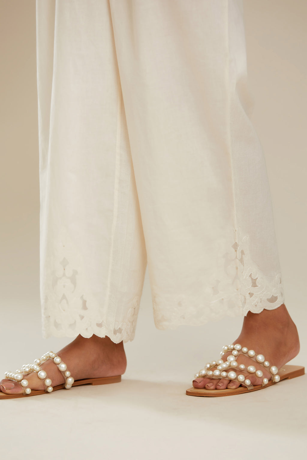 Off white cotton straight pants with appliqué detail at hem, highlighted with sequins. (Pants)
