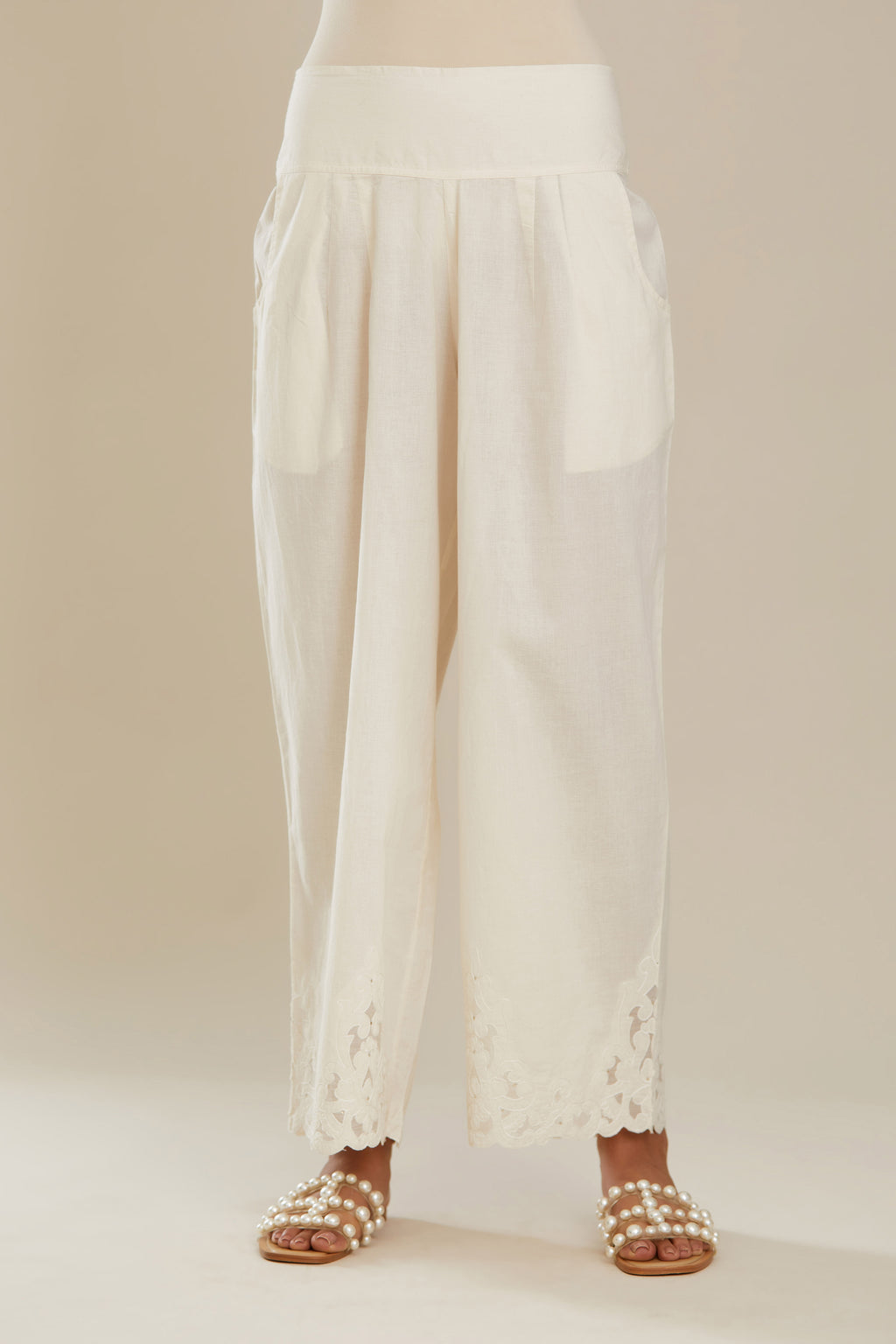 Off white cotton straight pants with appliqué detail at hem, highlighted with sequins. (Pants)