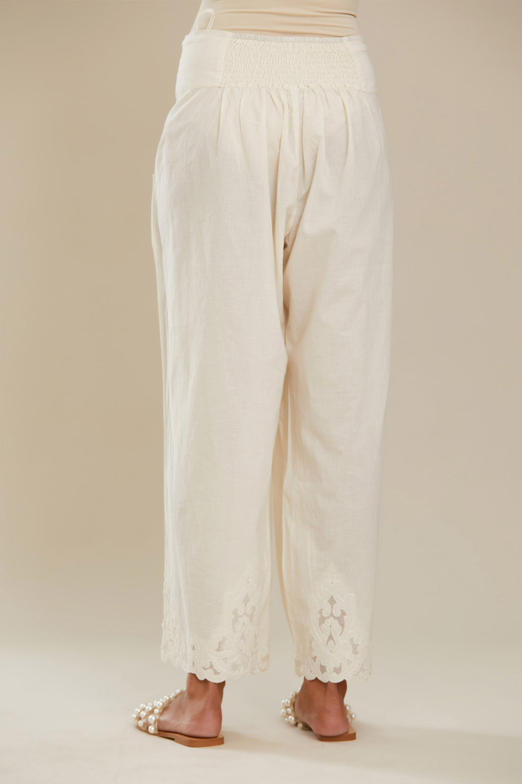 Off white cotton straight pants with appliqué detail at hem, highlighted with sequins. (Pants)