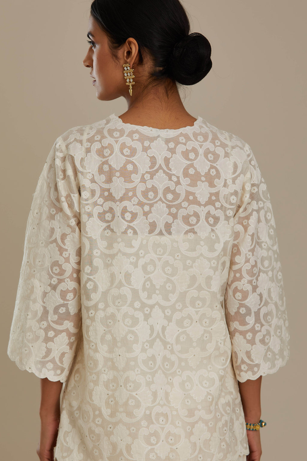 Off white cotton chanderi short top with all-over appliqué, highlighted with sequin, paired with off white cotton straight pants with appliqué detail at hem, highlighted with sequins.