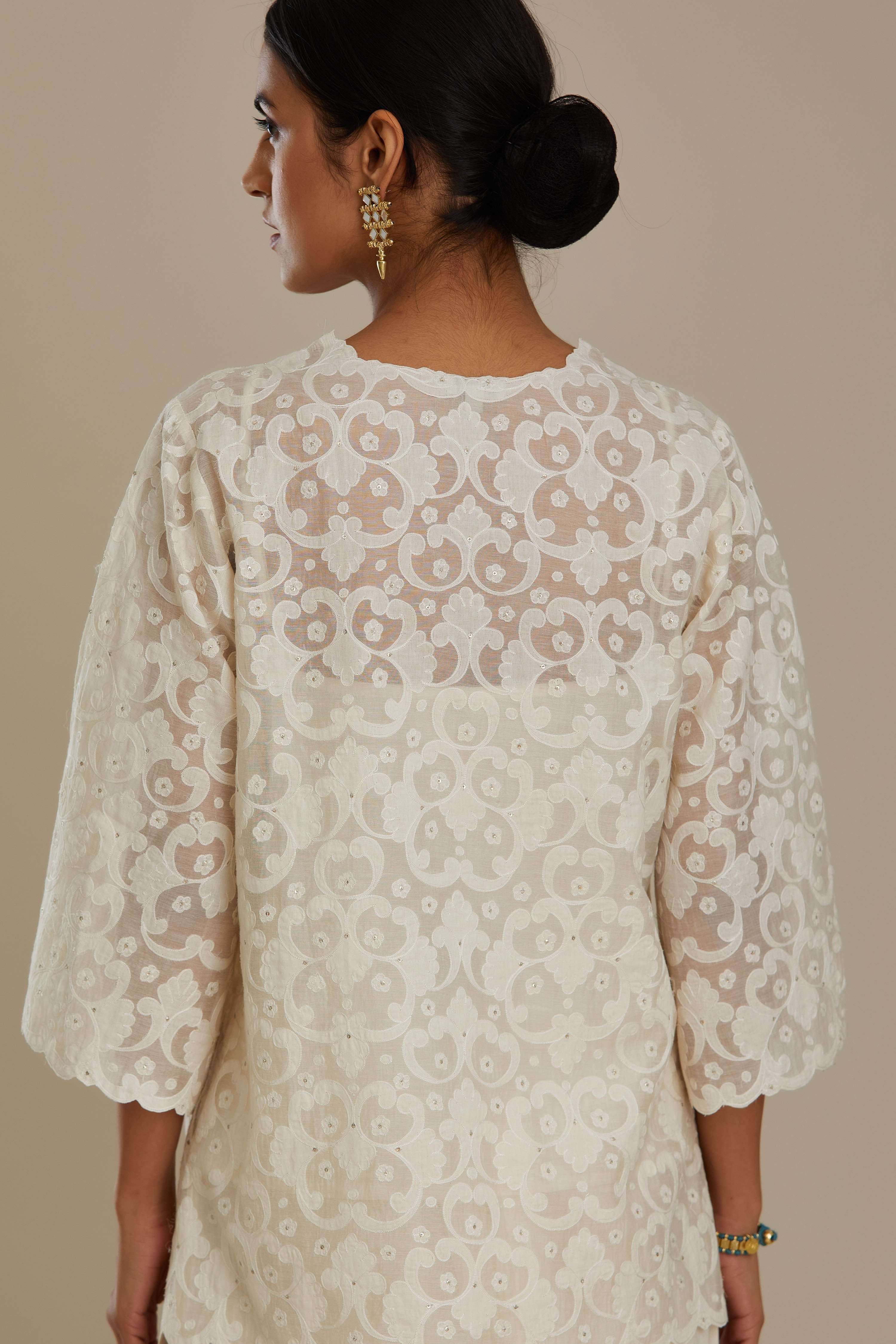 Off white cotton chanderi short top with all-over appliqué, highlighted with sequin, paired with off white cotton straight pants with appliqué detail at hem, highlighted with sequins.
