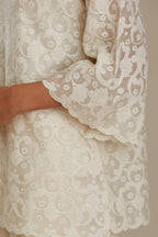 Off white cotton chanderi short top with all-over appliqué, highlighted with sequin, paired with off white cotton straight pants with appliqué detail at hem, highlighted with sequins.