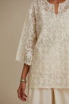 Off white cotton chanderi short top with all-over appliqué, highlighted with sequin, paired with off white cotton straight pants with appliqué detail at hem, highlighted with sequins.