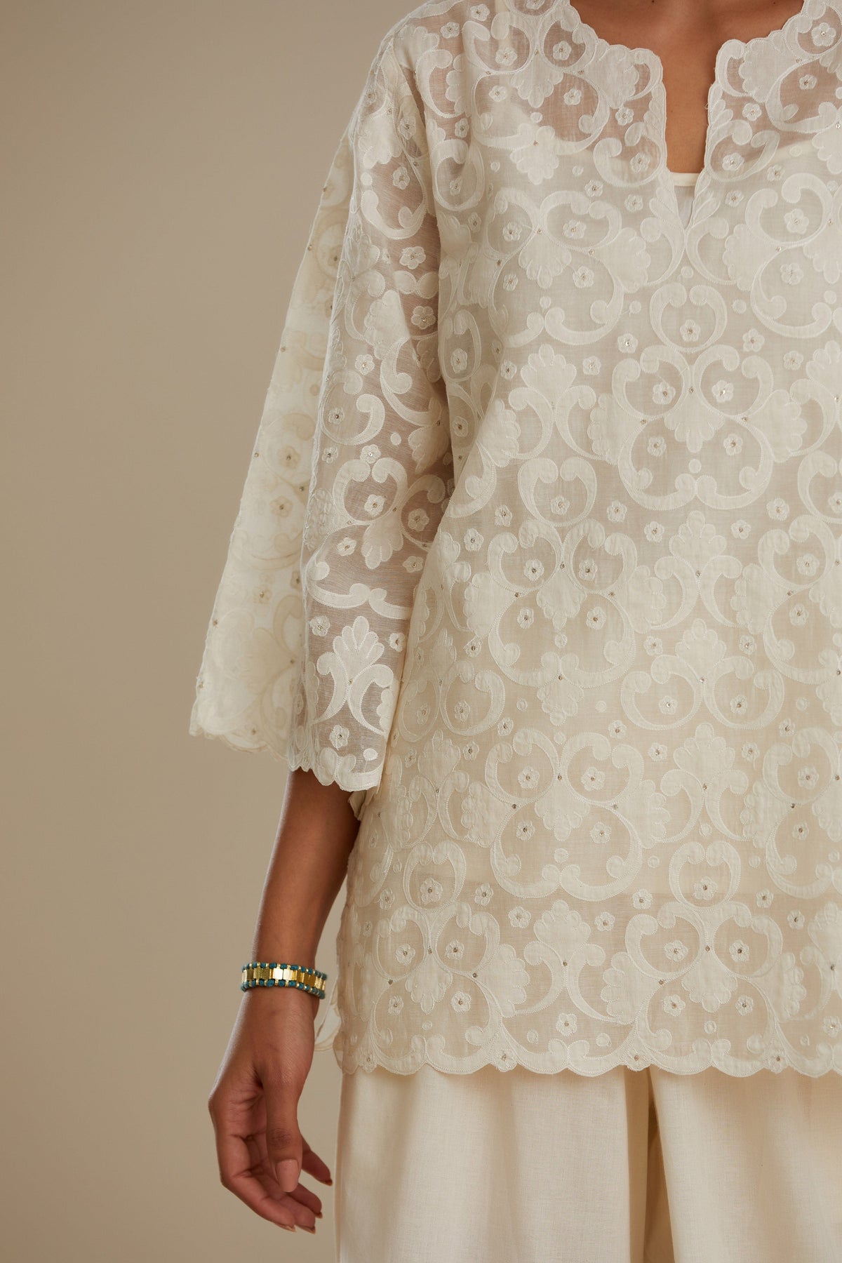 Off white cotton chanderi short top with all-over appliqué, highlighted with sequin, paired with off white cotton straight pants with appliqué detail at hem, highlighted with sequins.