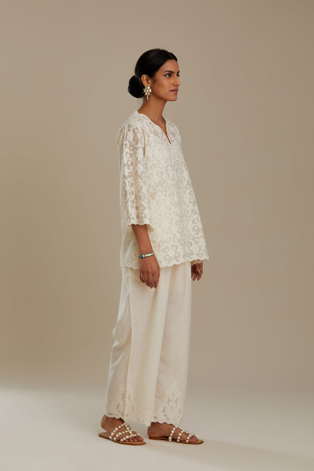 Off white cotton chanderi short top with all-over appliqué, highlighted with sequin, paired with off white cotton straight pants with appliqué detail at hem, highlighted with sequins.