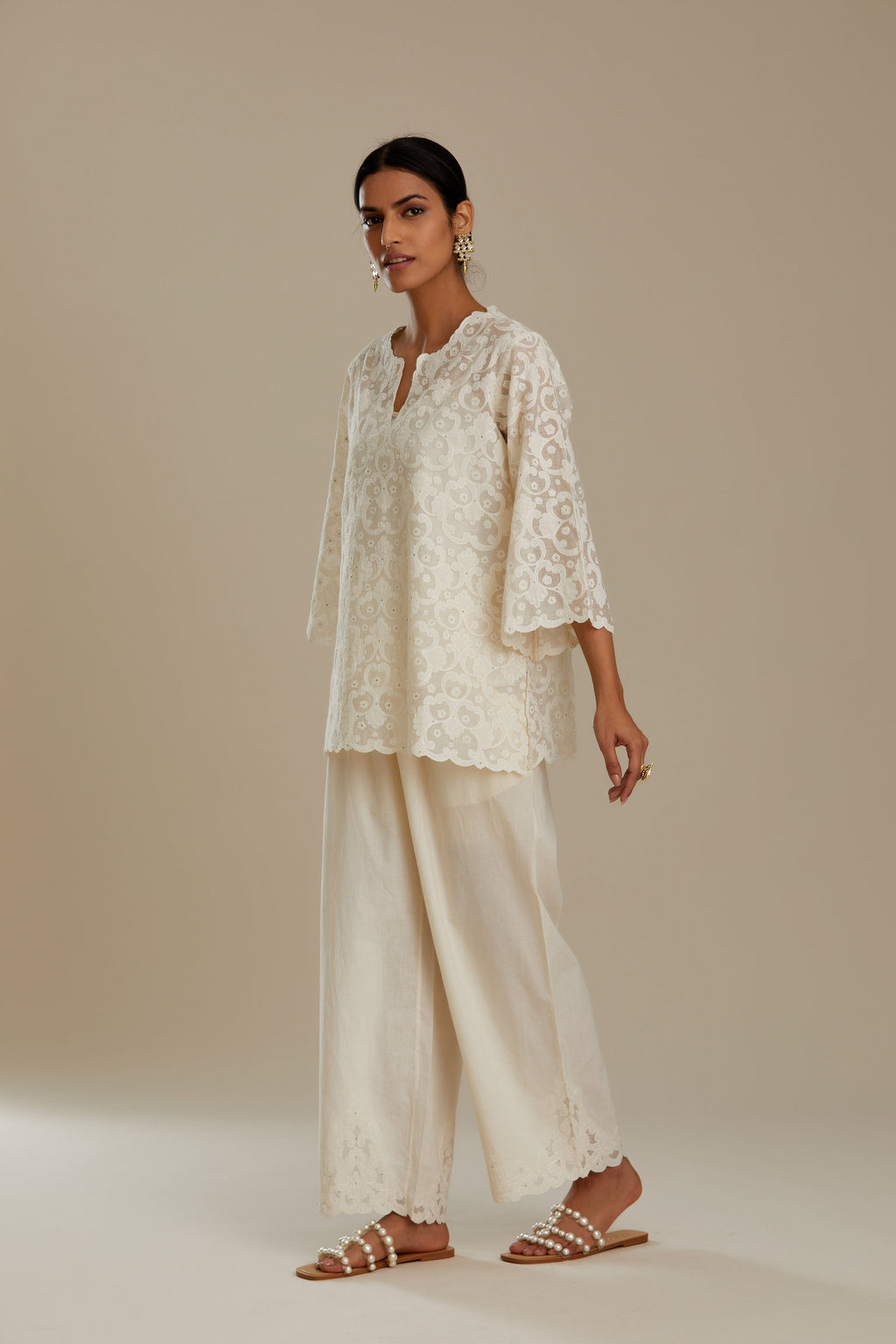 Off white cotton chanderi short top with all-over appliqué, highlighted with sequin, paired with off white cotton straight pants with appliqué detail at hem, highlighted with sequins.