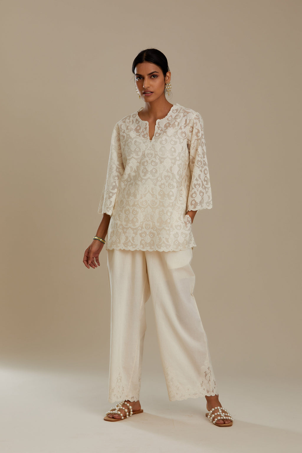 Off white cotton chanderi short top with all-over appliqué, highlighted with sequin, paired with off white cotton straight pants with appliqué detail at hem, highlighted with sequins.