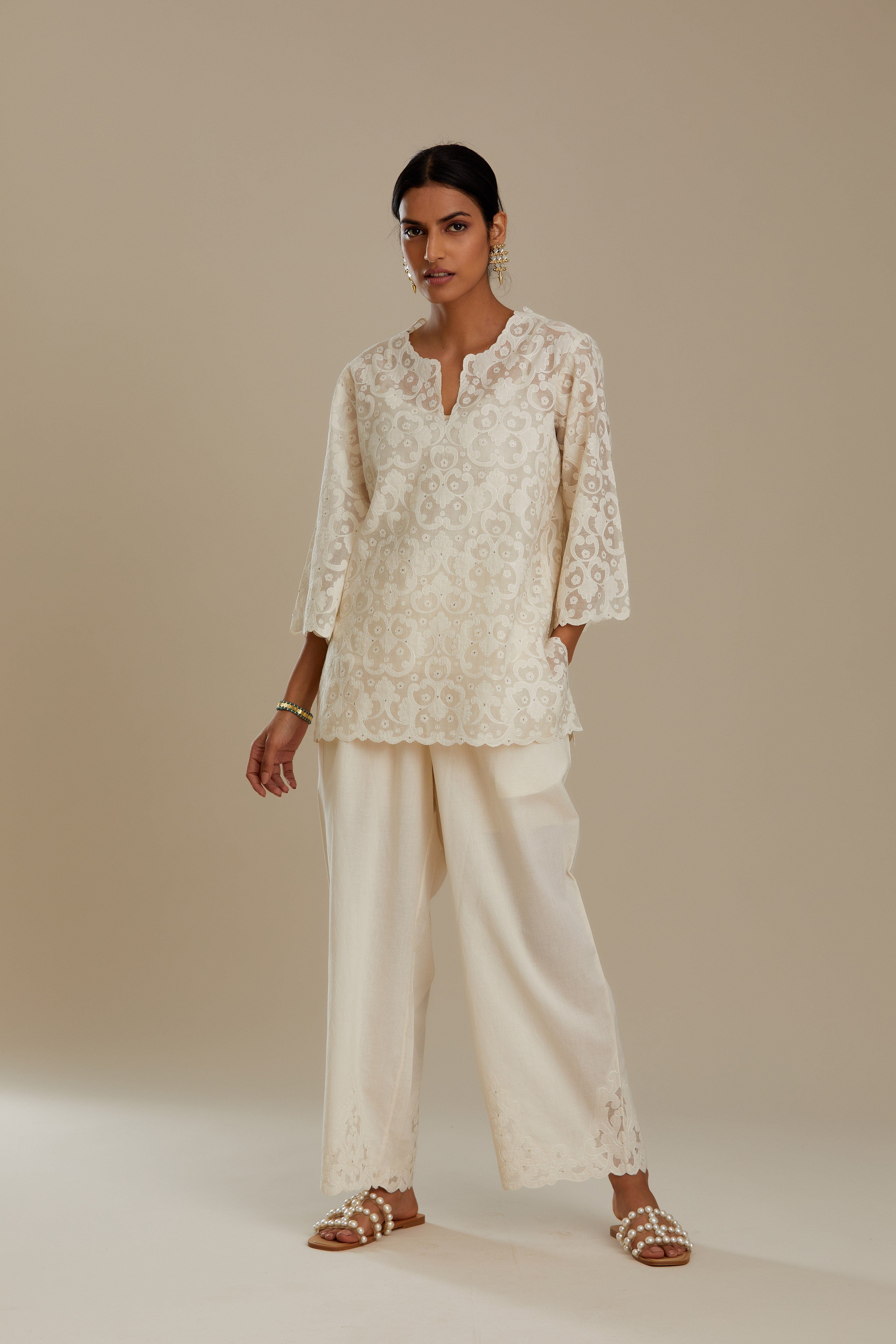 Off white cotton chanderi short top with all-over appliqué, highlighted with sequin, paired with off white cotton straight pants with appliqué detail at hem, highlighted with sequins.