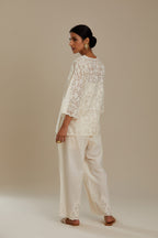 Off white cotton chanderi short top with all-over appliqué, highlighted with sequin, paired with off white cotton straight pants with appliqué detail at hem, highlighted with sequins.