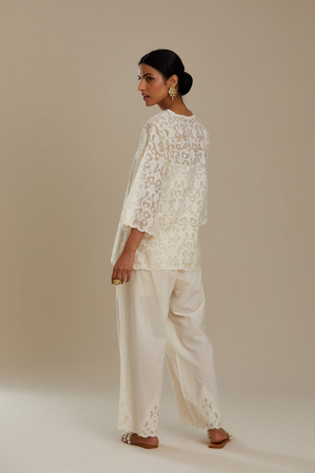 Off white cotton chanderi short top with all-over appliqué, highlighted with sequin, paired with off white cotton straight pants with appliqué detail at hem, highlighted with sequins.