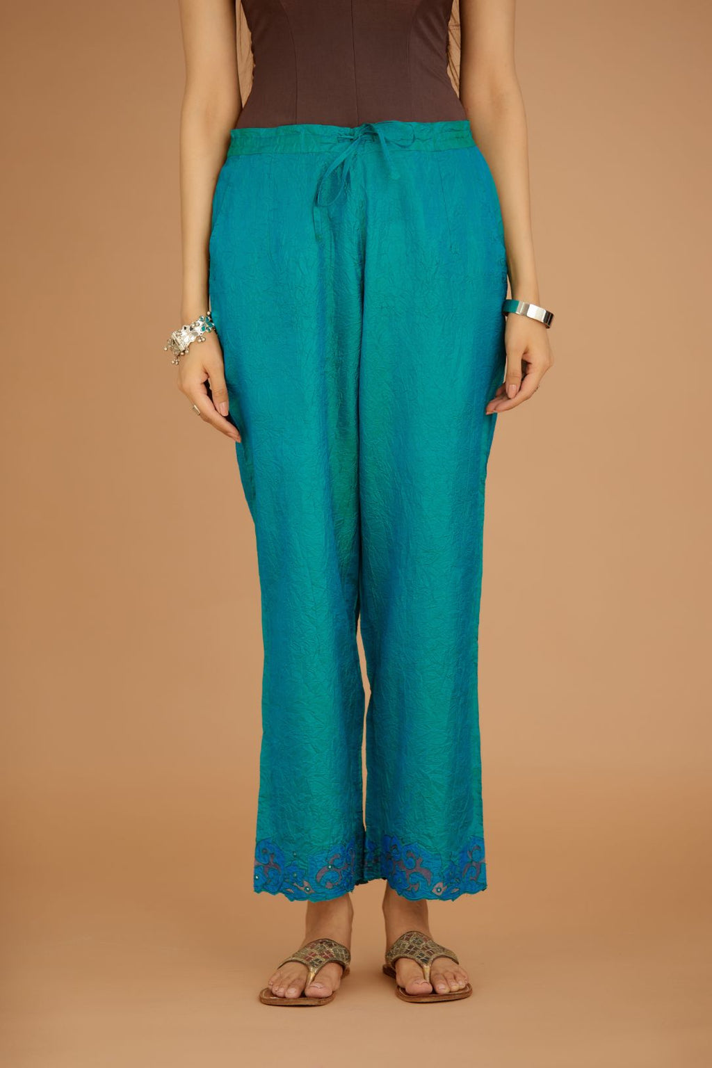 Teal blue hand crushed silk pants with contrast silk and organza fabric cutwork embroidery at bottom hem, highlighted with hand attached mirrors.