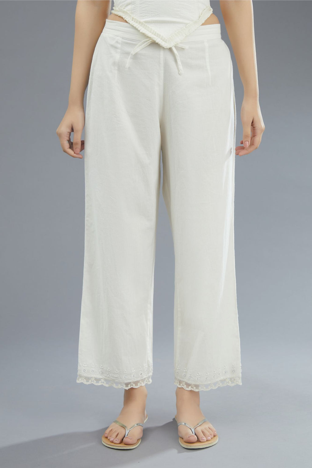 Off white straight pants detailed with lace and embroidery at bottom.