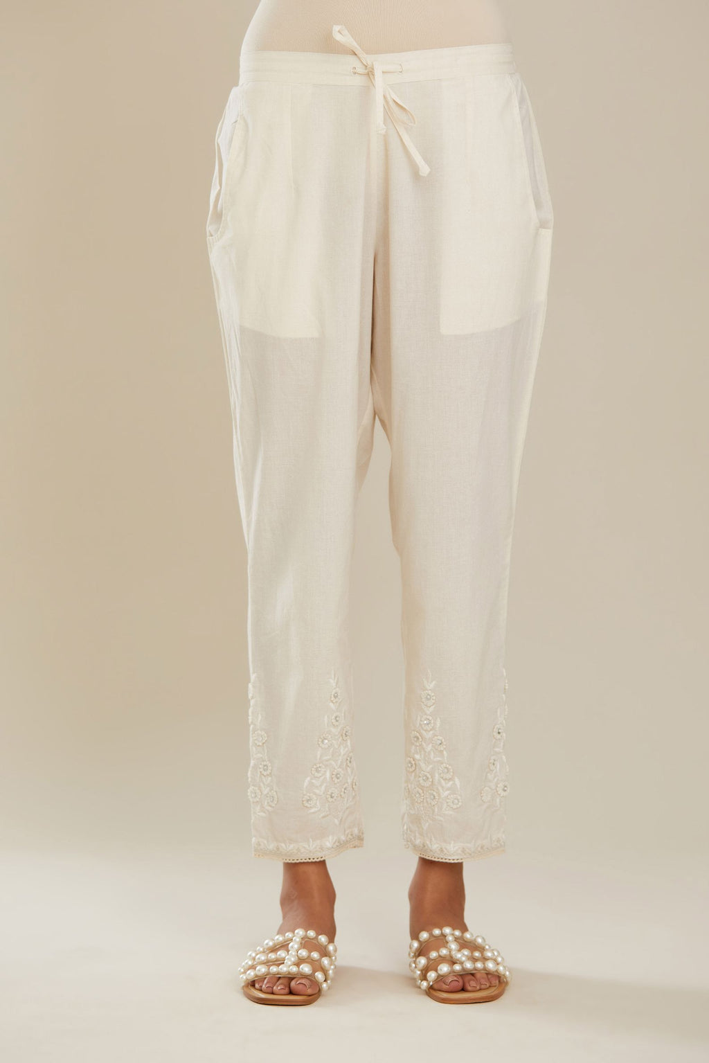 Off white cotton narrow pants with 3d embroidered flower boota at hem, highlighted with hand attached sequin and beads. Bottom hem edged with  lace. (Pants)