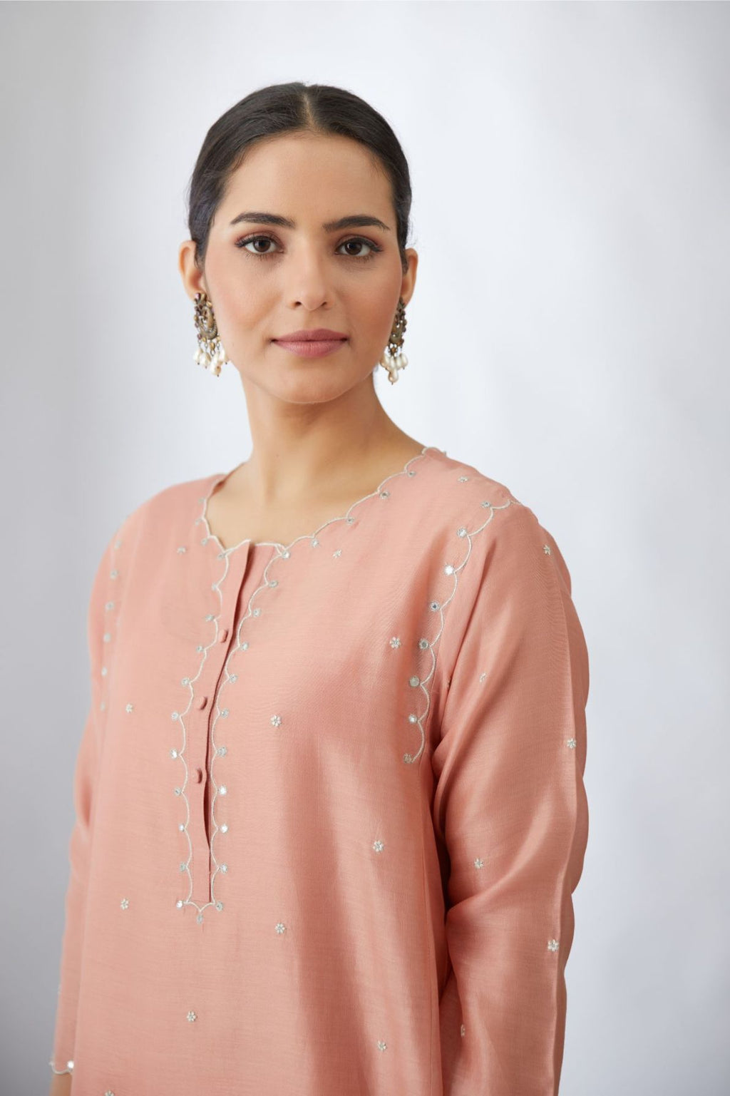 Salmon short kalidar kurta set with all-over delicately embroidered silver zari flowers and scalloped edges, highlighted with mirror hand work.
