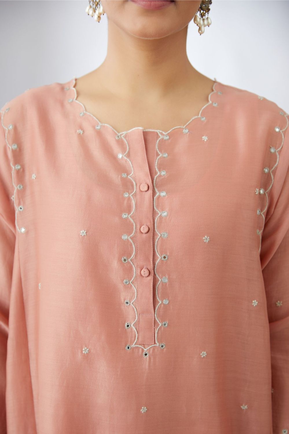 Salmon short kalidar kurta set with all-over delicately embroidered silver zari flowers and scalloped edges, highlighted with mirror hand work.
