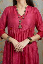 Fuchsia hand-crushed silk kurta set with wavy empire waistline and gathers, highlighted with beaded tassels and pulled thread embroidery.