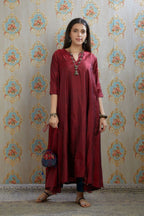 Asymmetric hem maroon hand crushed silk kurta highlighted with beaded tassels, paired with hand crushed straight silk pants.