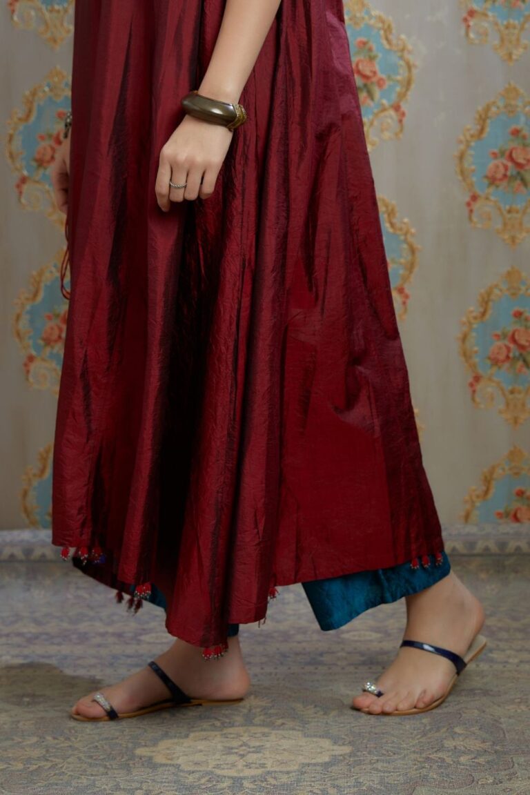 Asymmetric hem maroon hand crushed silk kurta highlighted with beaded tassels, paired with hand crushed straight silk pants.